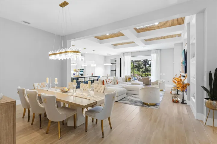 Bright, expansive open-concept living and dining areas featuring soaring ceilings, a coffered ceiling with inset wood trim, elegant architectural details, and expansive windows that fill the home with natural light.