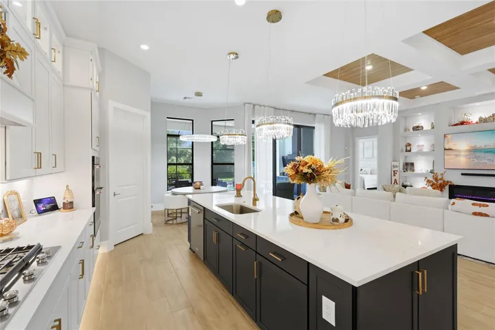 The gourmet kitchen boasts a 48-inch built-in KitchenAid refrigerator, double-stacked cabinetry with illuminated glass-front doors, wall oven and microwave, cooktop, and a large quartz island with additional cabinets and shelving. The quartz countertops extends up as the backsplash for an elegant and seamless finish.