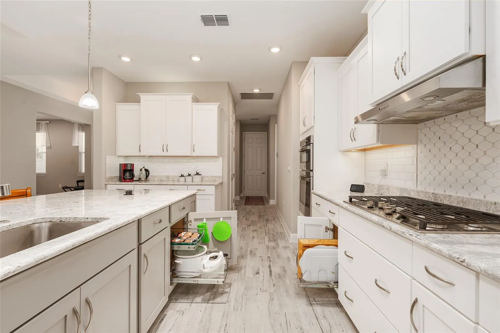 Thoughtfully designed kitchen featuring a large single-basin sink with built-in soap dispenser, convenient pull-out storage organizers, Cambria quartz countertops, and a decorative tile backsplash—combining functionality with everyday convenience.