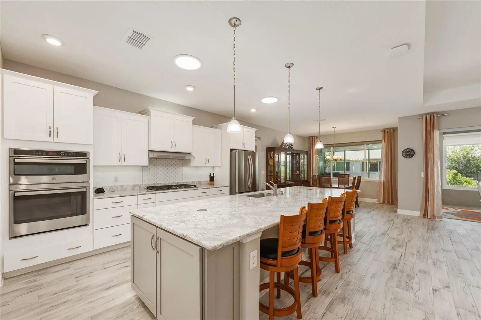 Beautifully appointed kitchen featuring an expansive Cambria quartz island with seating, staggered cabinetry, stainless steel appliances, GE double convection ovens with microwave, and two solar tubes that fill the space with natural light.