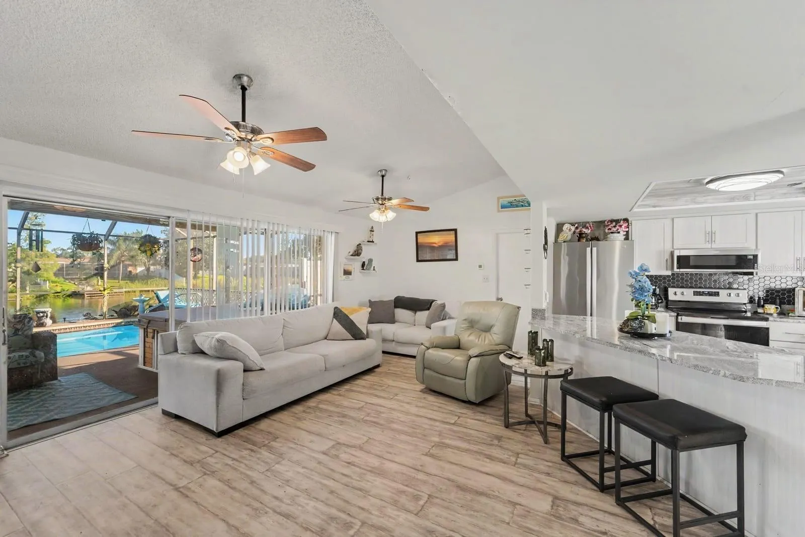 Open-concept living with pool view, modern kitchen, and ceiling fans