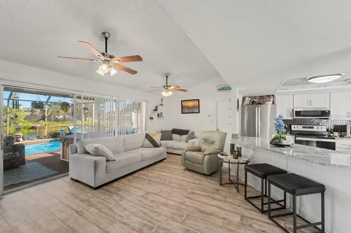 Open-concept living with pool view, modern kitchen, and ceiling fans