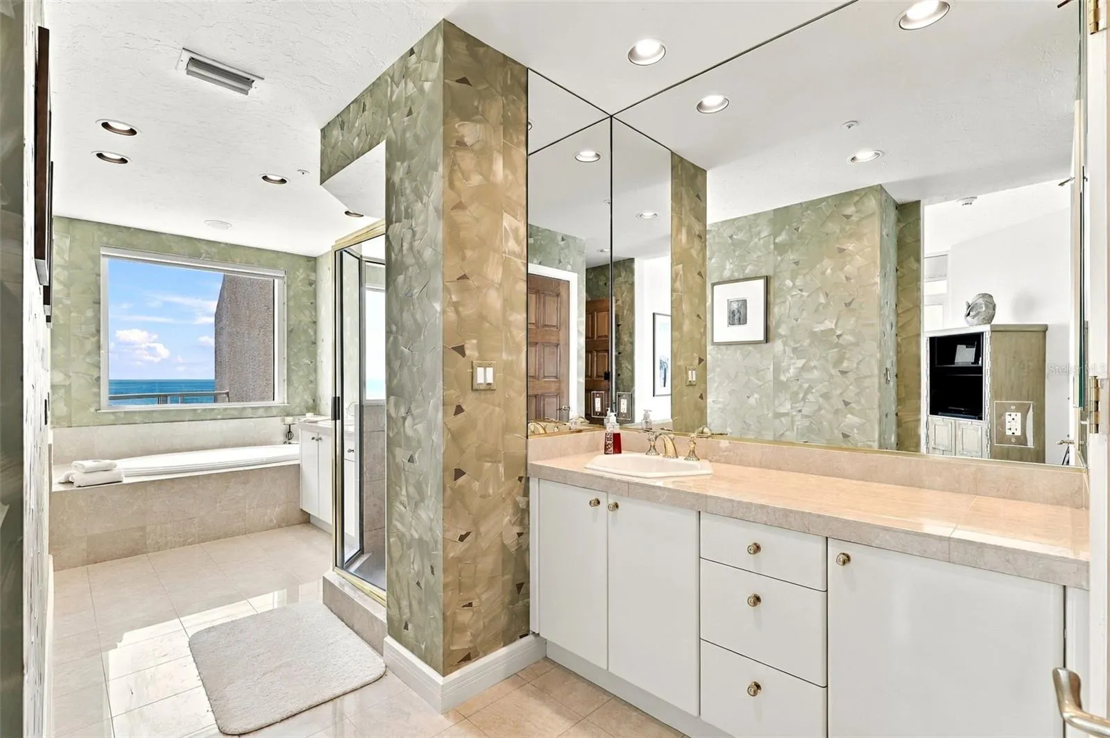 The primary ensuite bathroom offers dual vanities, marble floors and a huge spa tub overlooking the water and beach view.