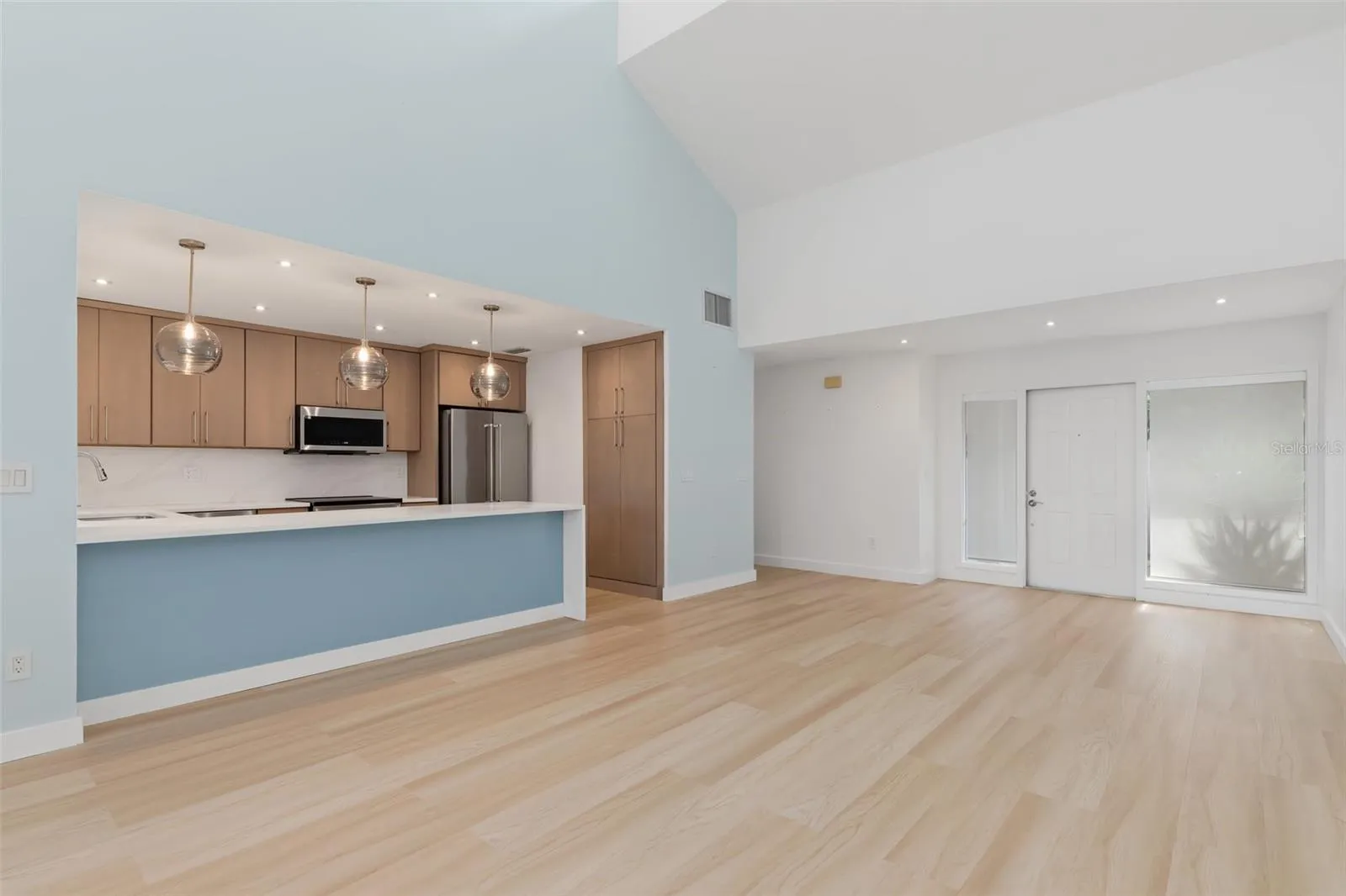 Great room unfurnished.  Kitchen breakfast bar with lighted blue glass face, modern cabinetry and pendant lighting.