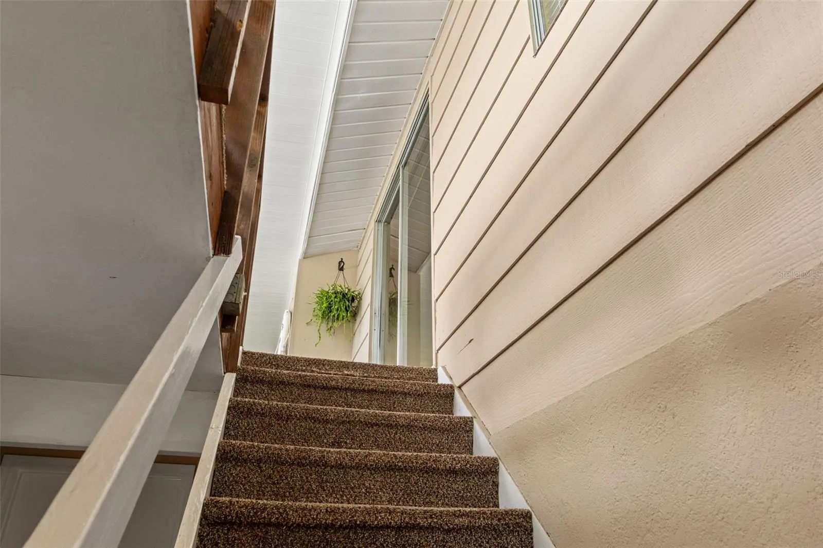 A carpeted stairway connects the elevated upper living area with the lower level. This view highlights the home's distinctive two-level design and access to the screened upper porch.