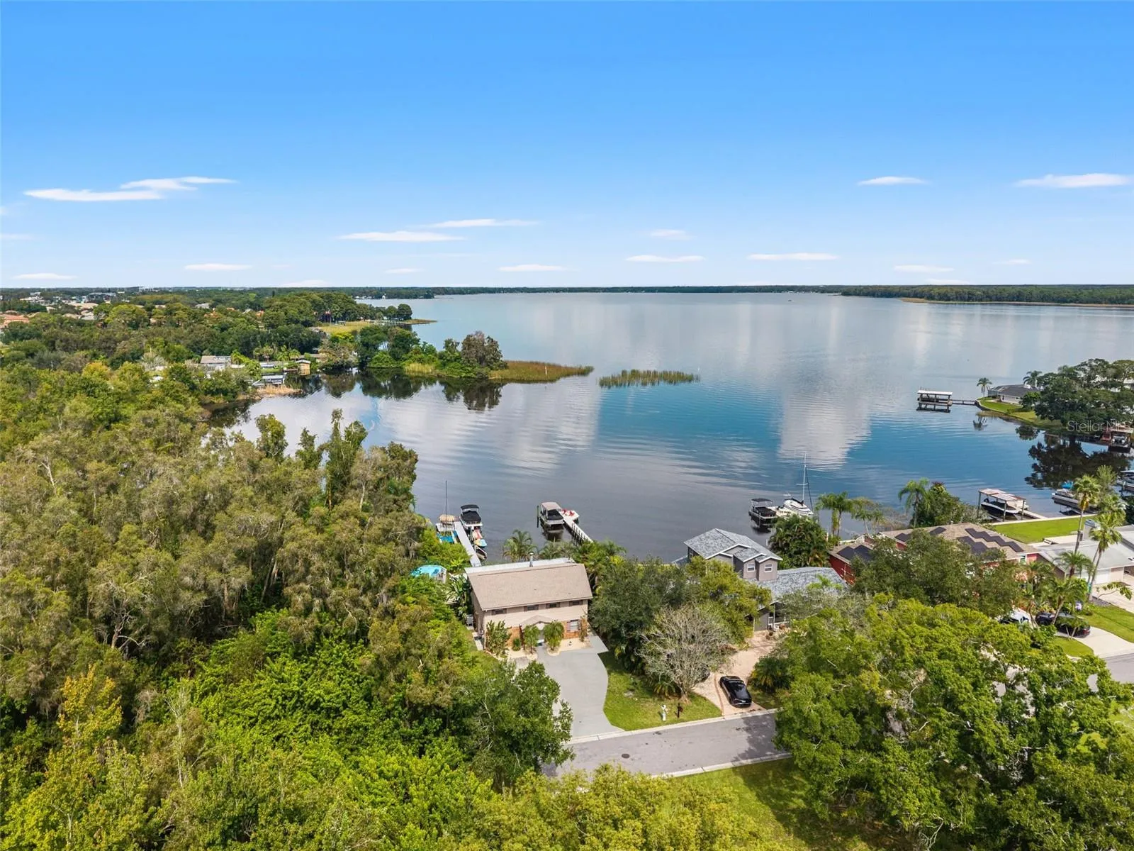 This aerial view captures the home's waterfront setting, with a private dock extending into the lake and mature trees surrounding the property. The natural shoreline, neighboring docks, and wide-open water create a beautiful backdrop for Florida lakefront living.