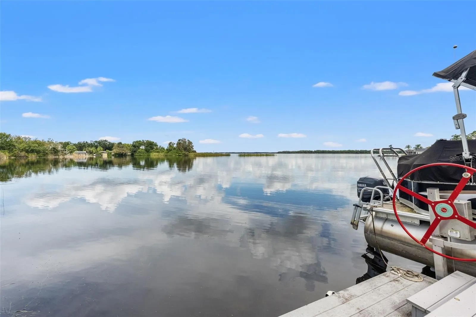Beautiful reflections dance across the lake in this wide-open waterfront view. Natural vegetation along the shoreline adds to the peaceful setting, while the dock provides a front-row seat to the surrounding scenery.