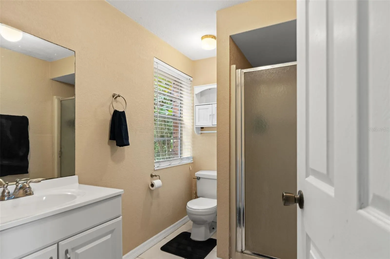 This lower-level bathroom features a white vanity, a walk-in shower with frosted glass enclosure, and a window that welcomes natural light. Conveniently located near the kitchenette and living area, it adds functionality to the home's flexible downstairs layout.