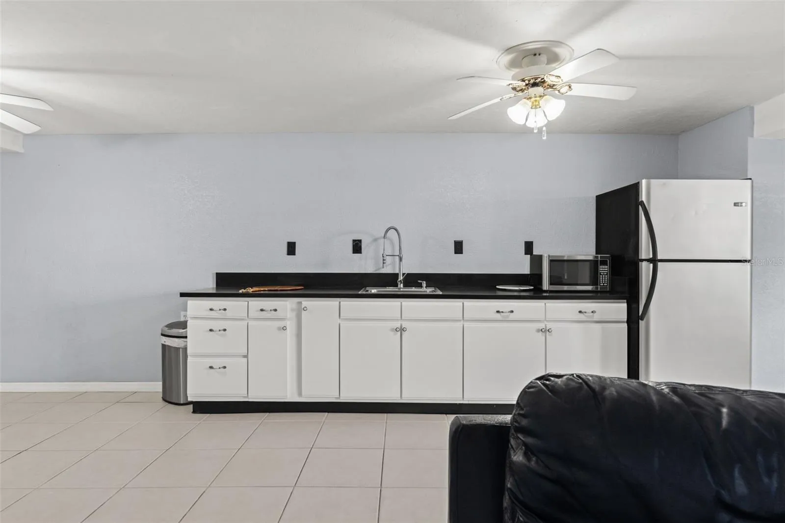 A closer look at the lower-level kitchenette reveals generous cabinet storage, dark countertops, a stainless-steel sink, refrigerator, and microwave. This additional food preparation area makes it easy to accommodate guests or enjoy snacks and refreshments without heading upstairs.