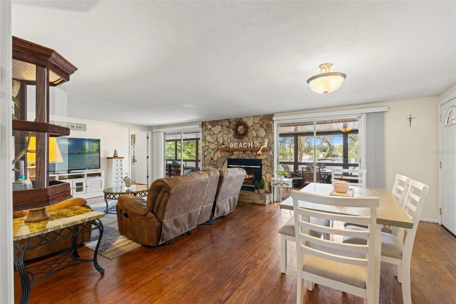 Waterfront views take center stage! The open living and dining areas feature beautiful wood flooring, a floor-to-ceiling stone fireplace, and sliding glass doors overlooking the water. Two separate screened outdoor spaces extend the living area.