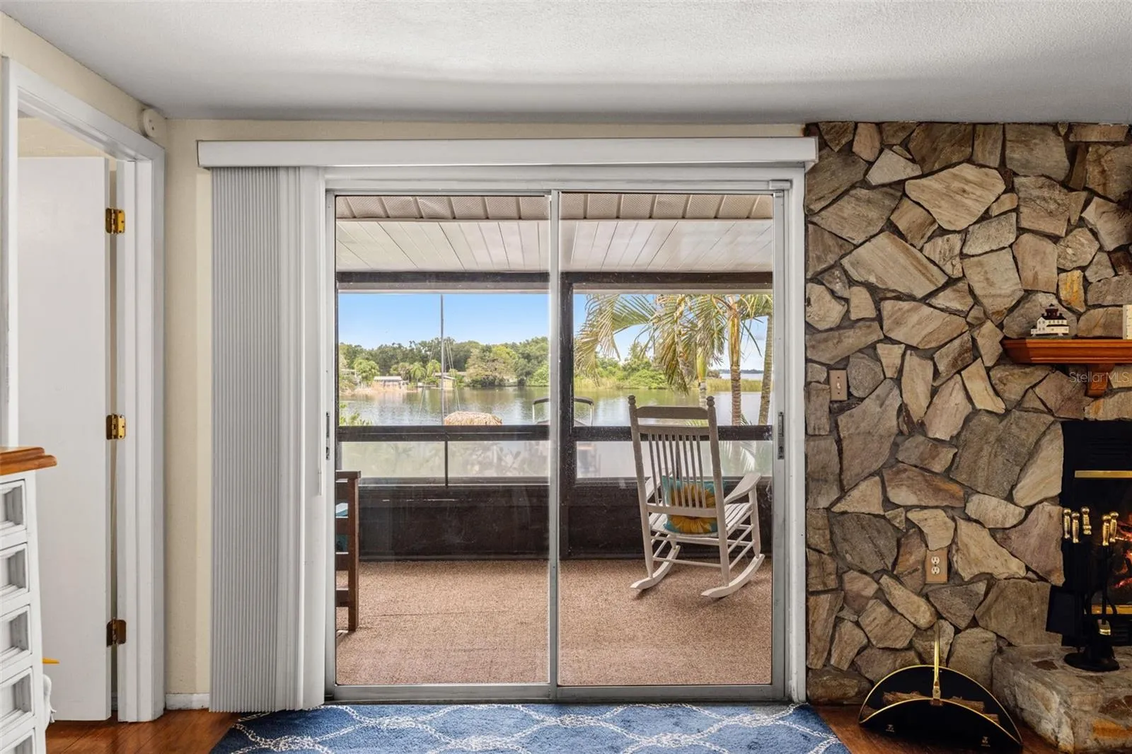 A fireplace with character! The floor-to-ceiling stone surround creates a distinctive focal point, while sliding glass doors bring in natural light and connect the living room to a screened outdoor space overlooking the water.