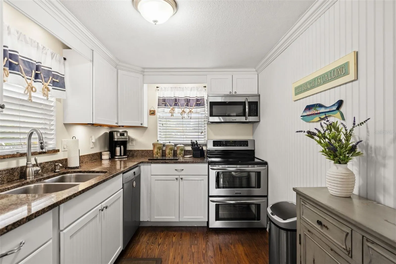 Thoughtfully arranged for everyday convenience, the kitchen features a double-basin sink, stainless steel dishwasher, electric range with double ovens, built-in microwave, and ample cabinetry. Windows bring natural light into the space.