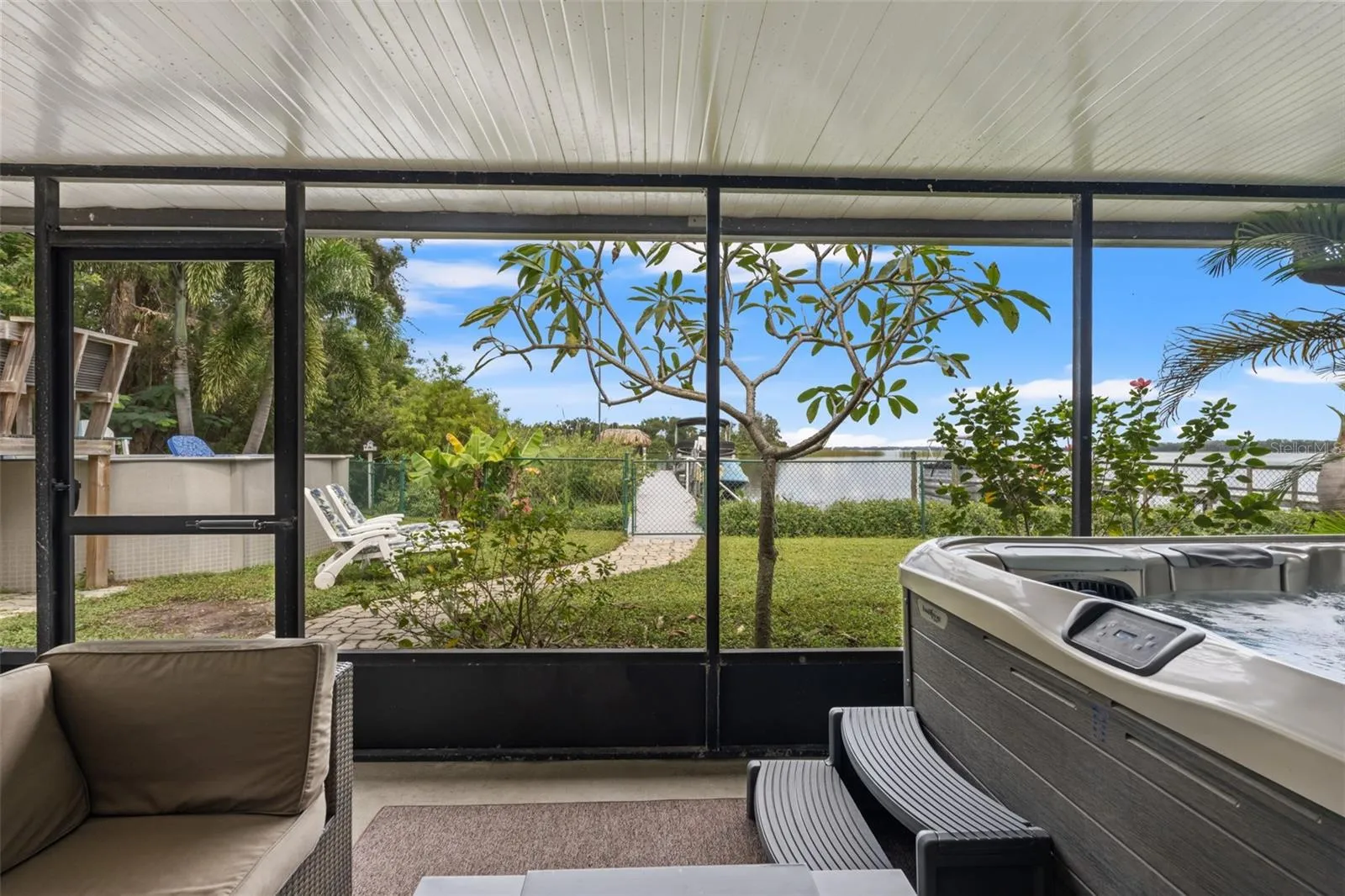 The lower-level screened patio overlooks a grassy backyard with a pathway leading toward the waterfront. Enjoy views of the dock and boats beyond, with additional outdoor recreation space just steps away.