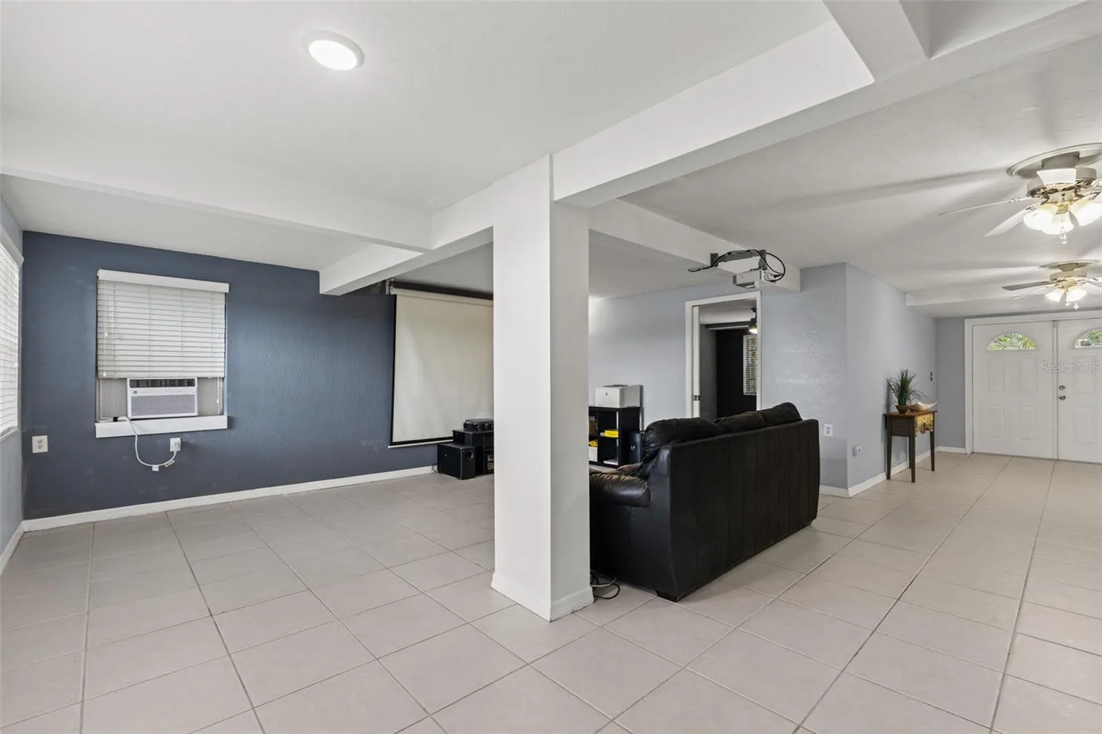 This wide-angle view highlights the versatility of the downstairs layout, with an open area adjoining the media room and easy access to the separate exterior entrance. Tile flooring runs throughout, providing a practical foundation for entertaining, recreation, or additional living space.