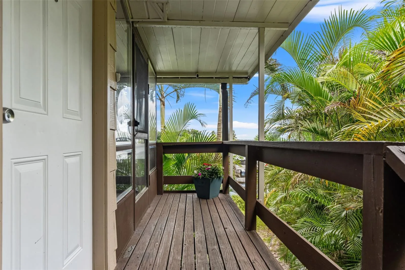 Surrounded by lush tropical palms, the covered upper-level entry offers a welcoming approach to the home, complete with wood decking, railings, and protection from the elements.