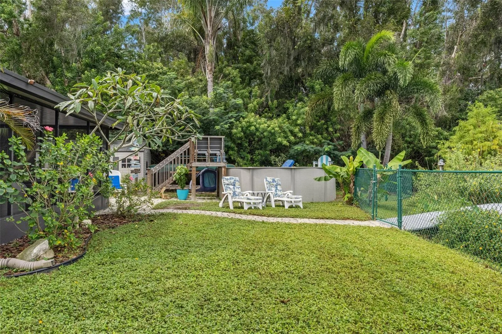 Enjoy your own backyard retreat with an above-ground pool, raised wooden deck, and surrounding lounge areas. Mature trees and tropical landscaping create a leafy backdrop, while the nearby lawn and paver walkway provide space to enjoy the outdoors.