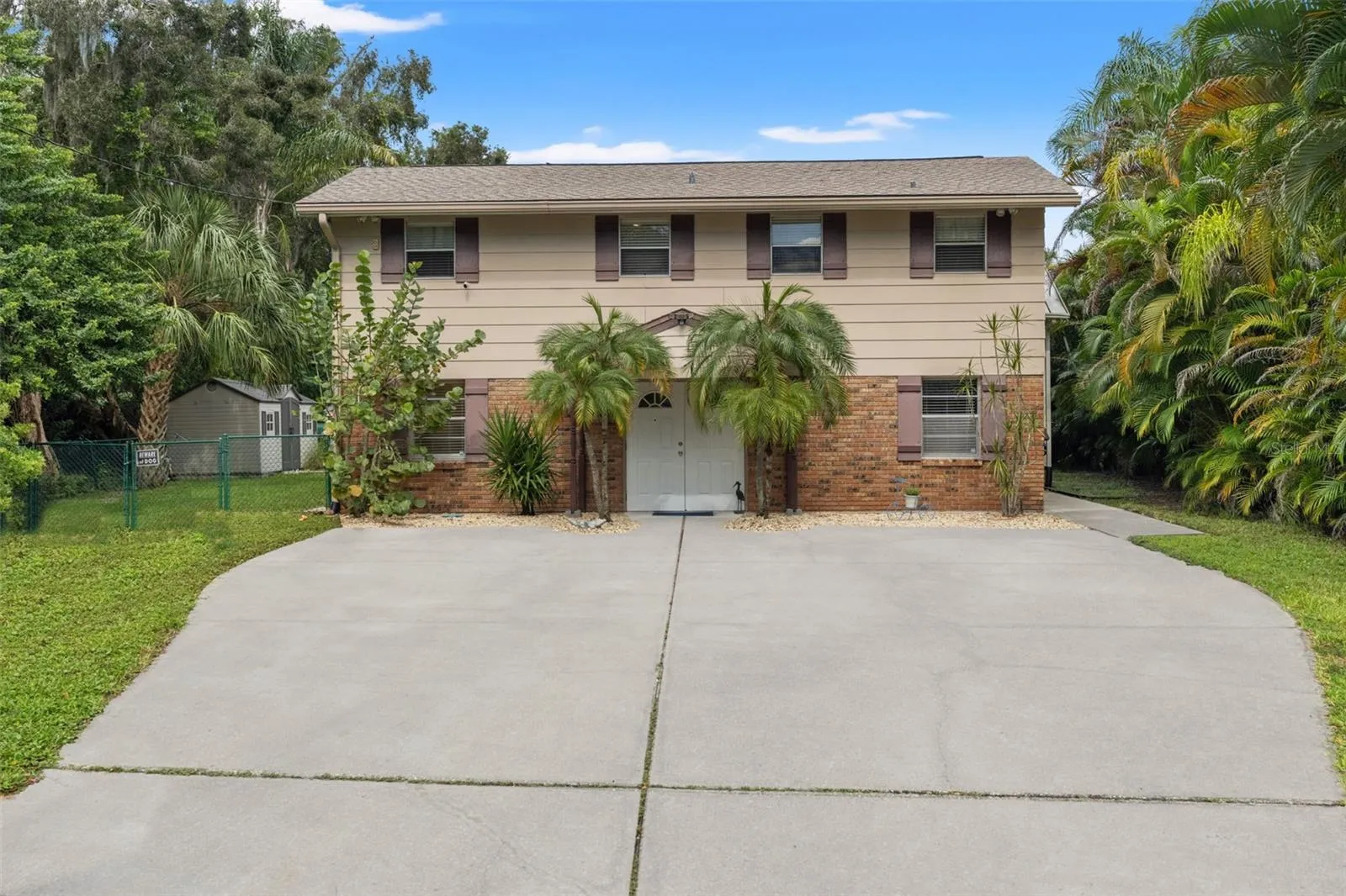 Welcome to 13 Freshwater Drive! This elevated waterfront home features a classic brick-and-siding exterior, mature tropical landscaping, and an expansive concrete driveway offering plenty of room for parking.