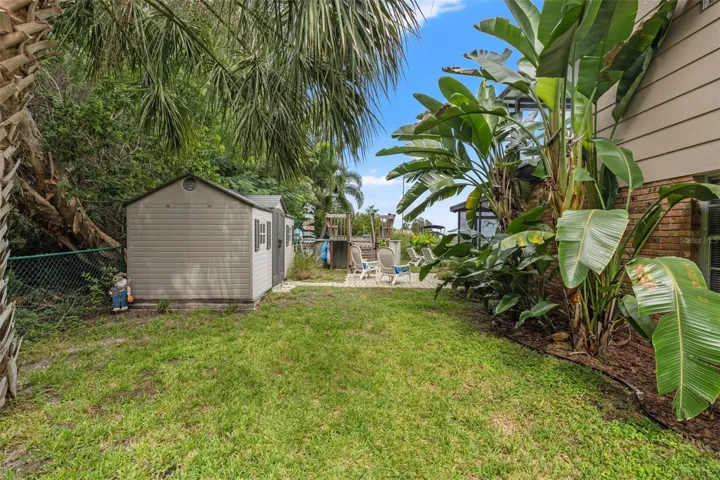 Tropical landscaping surrounds this spacious side yard, complete with a freestanding storage shed for outdoor equipment, tools, and recreational gear. The grassy area connects to the backyard's patio, pool, and waterfront amenities.