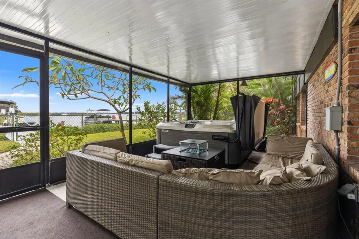 Your waterfront retreat continues downstairs! This spacious screened patio features a hot tub, comfortable sectional seating, and views toward the water. Surrounded by tropical landscaping, it's an inviting place to entertain or unwind after a day on the lake.