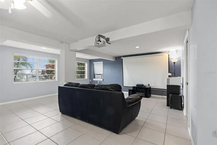 Movie nights have their own dedicated space! The lower-level living area is currently arranged as a home theater, complete with a large projection screen, ceiling-mounted projector, and comfortable seating. Multiple windows bring natural light into the room, making it equally suitable for everyday relaxation.