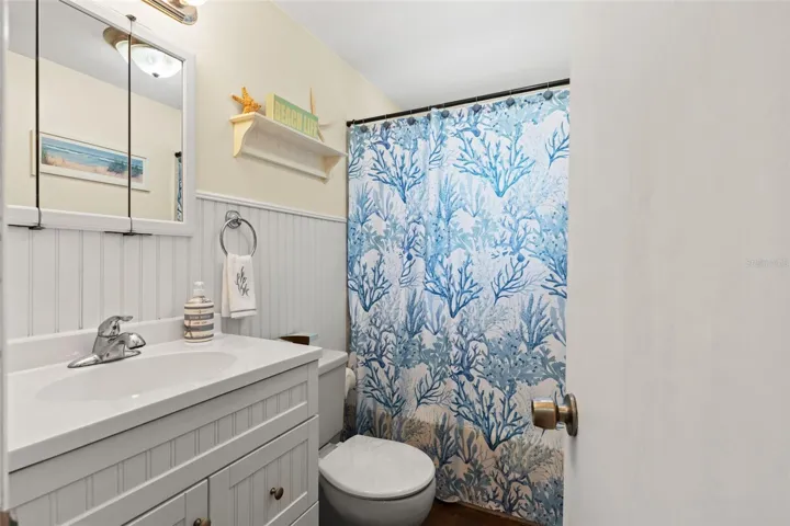 Coastal charm continues into this full bathroom, featuring a white vanity with decorative beadboard-style detailing, a mirrored medicine cabinet, and a tub/shower combination. White wainscoting and cheerful blue accents complete the beach-inspired look.