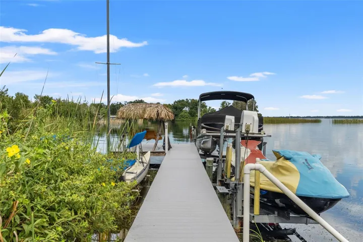 Your Florida boating lifestyle starts right here! The waterfront dock features a covered pontoon boat on a lift, personal watercraft lift, and space for additional recreational equipment. A thatched-roof seating area at the end of the dock offers a relaxing spot overlooking the lake.