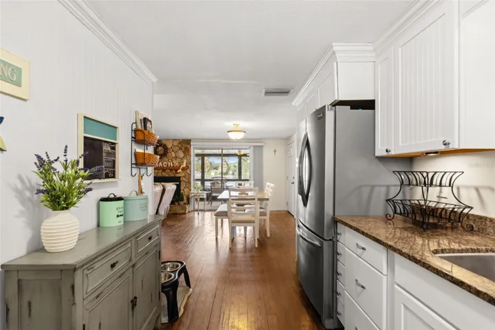 The kitchen opens directly to the dining and living areas, creating an easy flow throughout the upper level. White cabinetry, warm wood flooring, and a stainless steel refrigerator complement the home's relaxed coastal character.