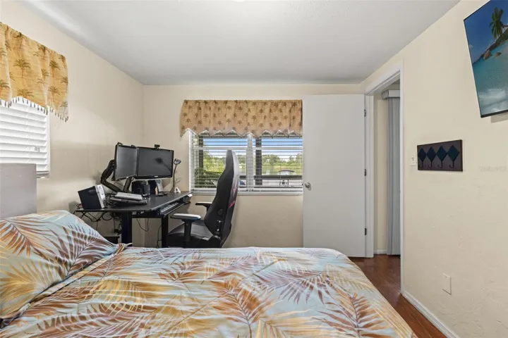 This versatile bedroom offers wood flooring, two windows for natural light, and a built-in closet. Currently arranged with both a bed and computer workstation, it demonstrates how easily the room accommodates sleeping and home office needs.