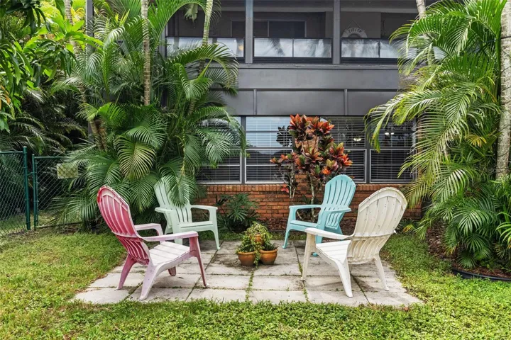 Tucked among lush palms and colorful tropical plants, this charming outdoor seating area offers another place to unwind. Four Adirondack-style chairs create a casual gathering spot beneath the home's elevated screened porch.