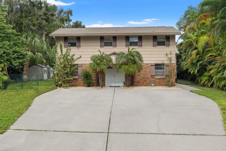 Welcome to 13 Freshwater Drive! This elevated waterfront home features a classic brick-and-siding exterior, mature tropical landscaping, and an expansive concrete driveway offering plenty of room for parking.