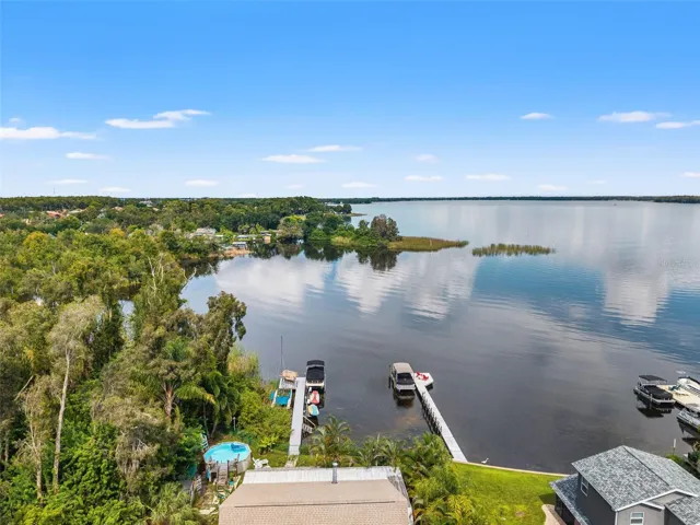 This aerial view showcases the home's waterfront location, private dock, and tropical backyard, including an above-ground pool. Mature landscaping provides a lush setting, while the lake opens into an impressive expanse of water just beyond the dock.