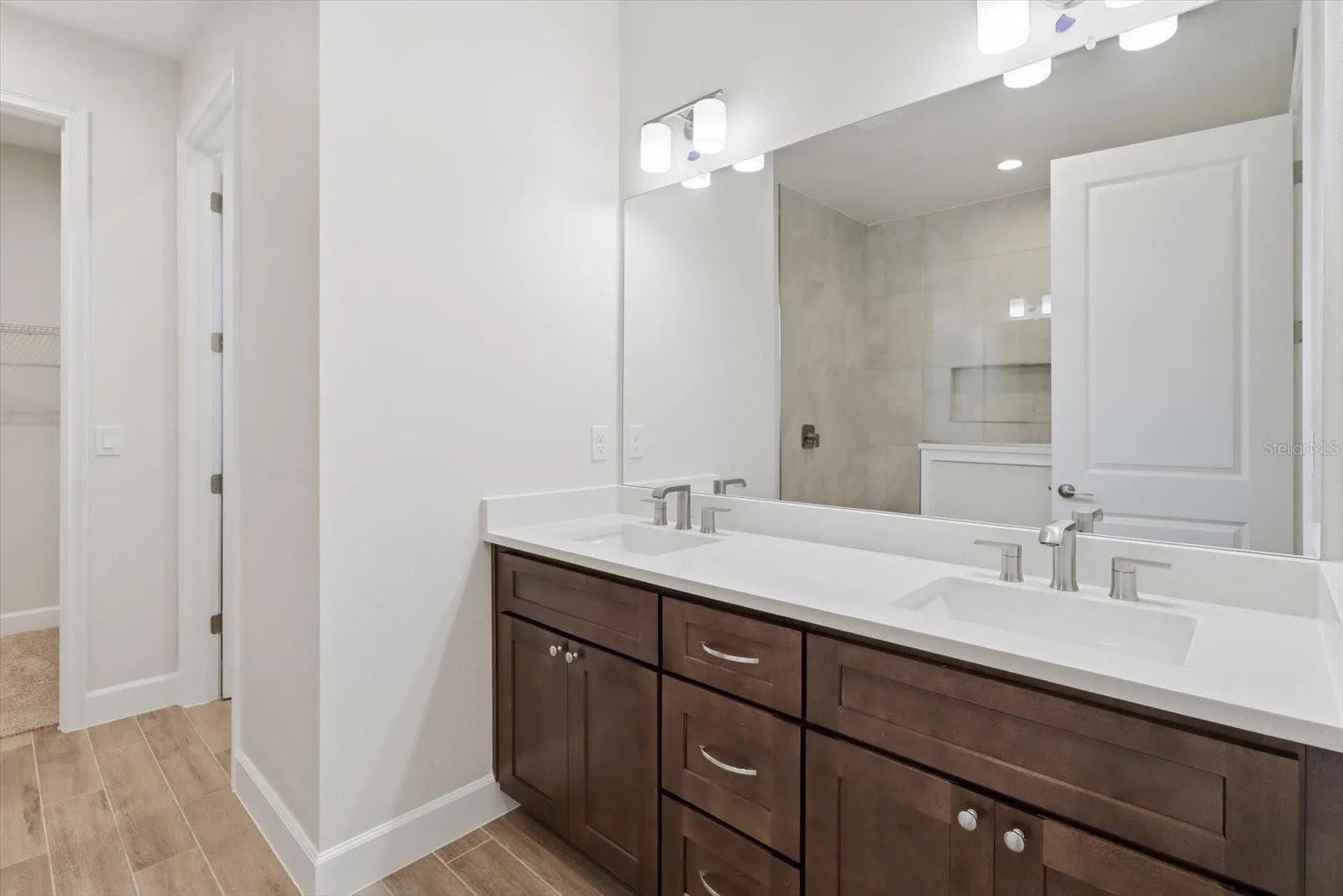 The primary bathroom has dual sinks, custom wood cabinets, and plank tile flooring.
