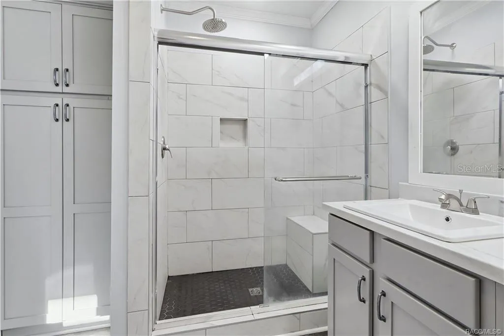 WALK-IN SHOWER features marble-look tile, a rainfall-style showerhead, glass sliding doors, built-in seating &amp; a convenient recessed niche.