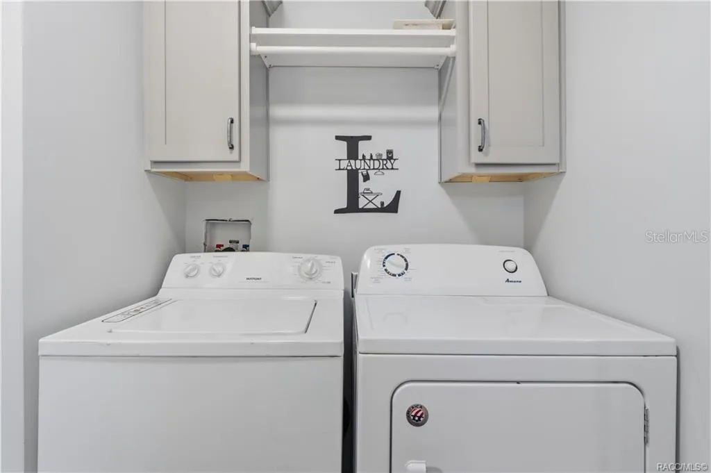 LAUNDRY MADE CONVENIENT! The INDOOR LAUNDRY AREA features a washer, dryer, overhead GRAY CABINETRY &amp; shelving for additional storage.