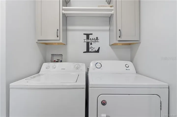 LAUNDRY MADE CONVENIENT! The INDOOR LAUNDRY AREA features a washer, dryer, overhead GRAY CABINETRY &amp; shelving for additional storage.