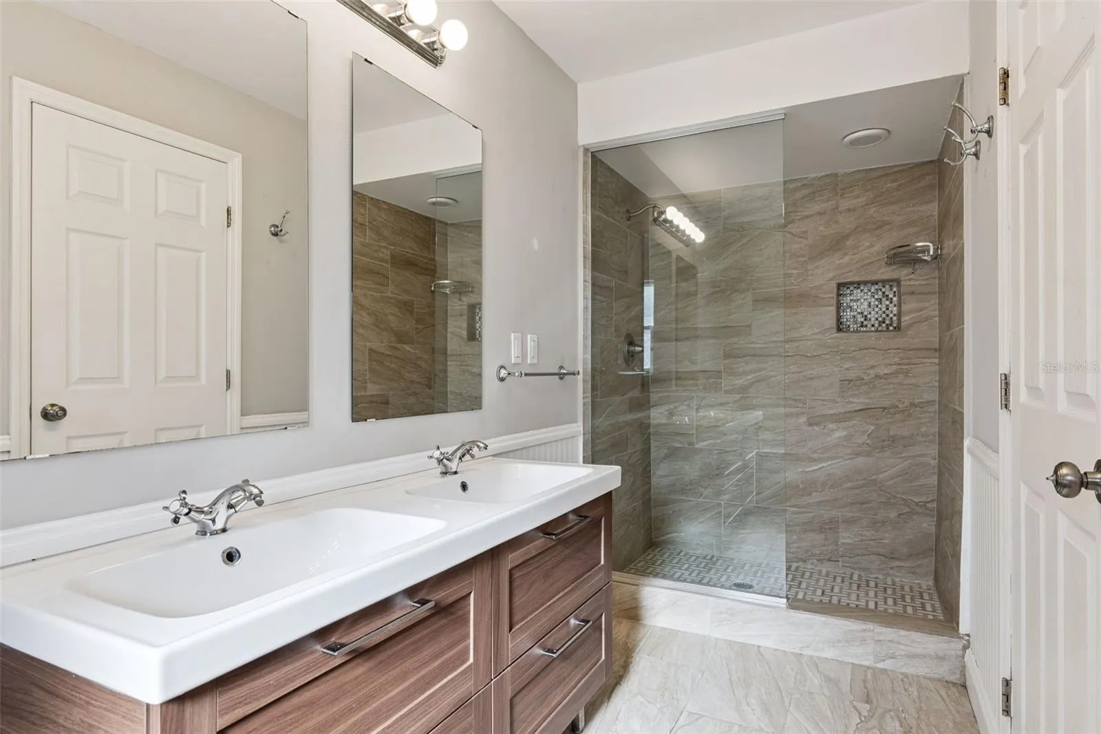 Tiled walk-in shower with a glass panel and dual sinks