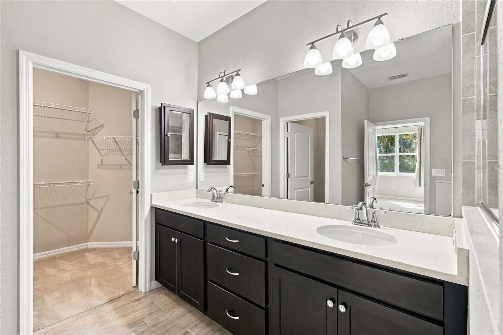 Double sink vanity with ample storage, medicine cabinet, and walk-in closet to the left