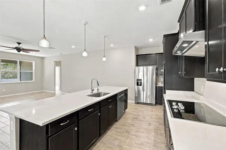 Kitchen with solid deep wood cabinets, quartz counters, and chic pendant lights - cooktop with range hood to the right