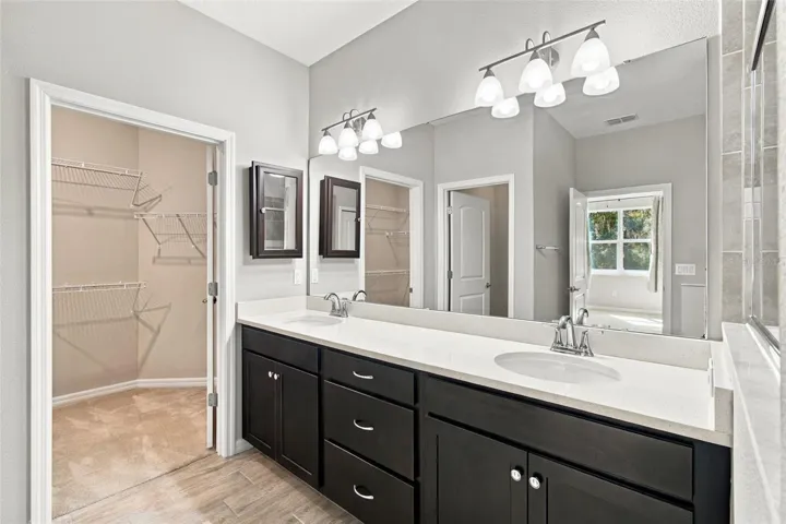 Double sink vanity with ample storage, medicine cabinet, and walk-in closet to the left