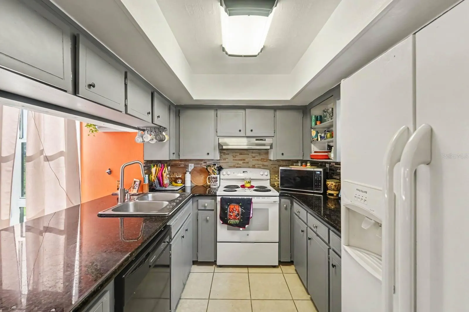 Galley kitchen features gray cabinetry, dark countertops &amp; brick backsplash