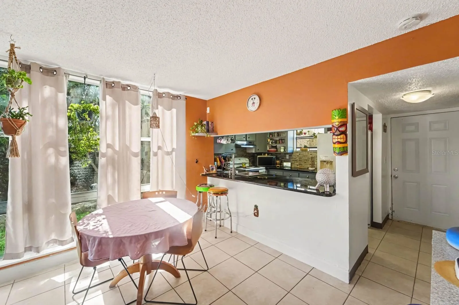 Spacious kitchen-dining combo with orange wall, white appliances &amp; pass-through counter