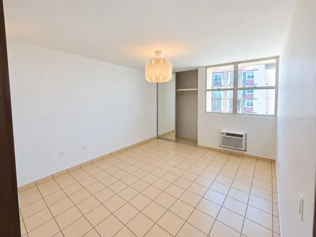 Primary bedroom with tile flooring, closet and wall-mounted air-conditioning unit.