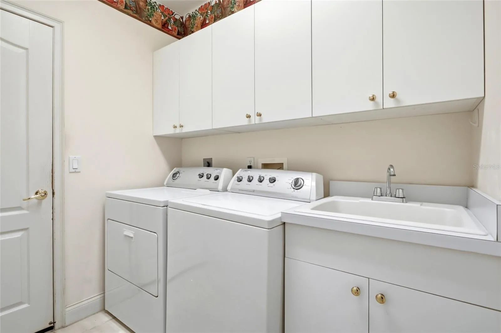 Indoor laundry room with overhead cabinets, a utility sink, and side-by-side appliance space.