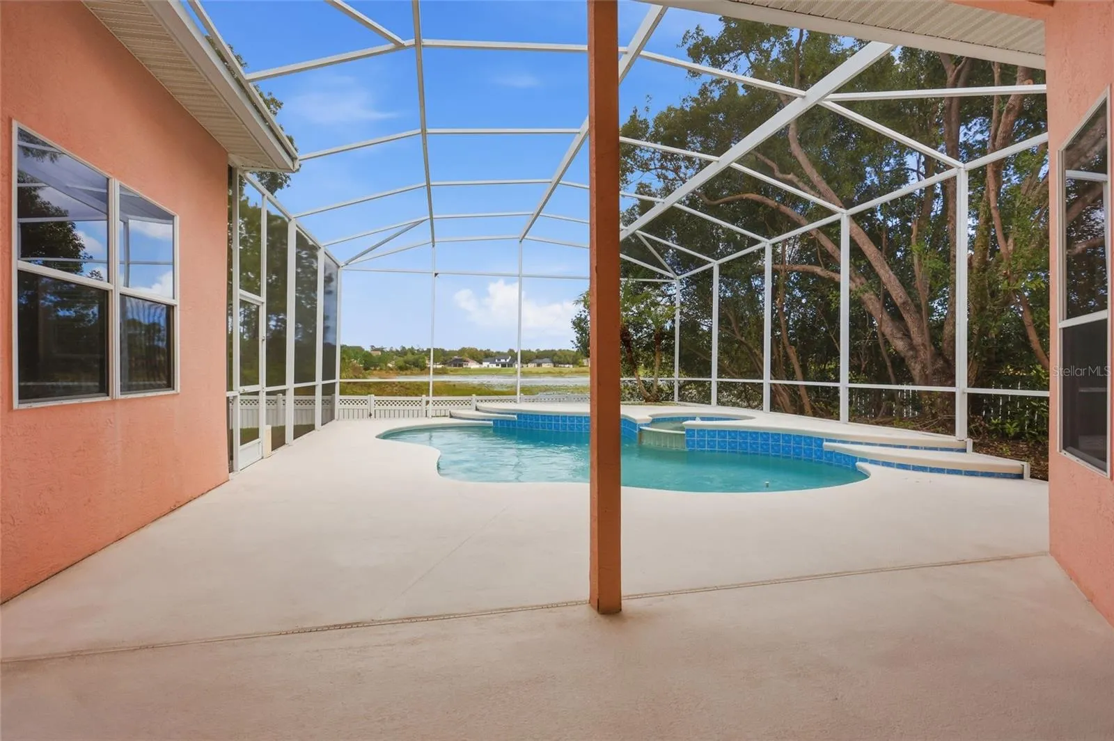 Large covered back porch overlooks the screened pool and lake, with space for outdoordining and shaded seating.