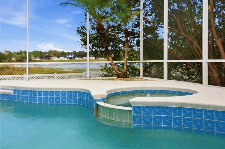 Integrated spa and blue pool tile frame the lake-view setting. The screened pool has a newpool pump.