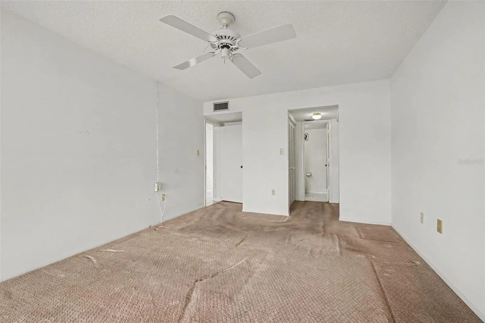 Primary bedroom with ceiling fan, carpet, and direct access to the en-suite bathroom.