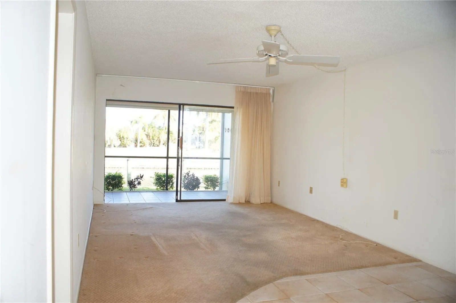 Living room with sliding glass doors opening to the screened lanai, ceiling fan, and natural light from the canal side of the condo.