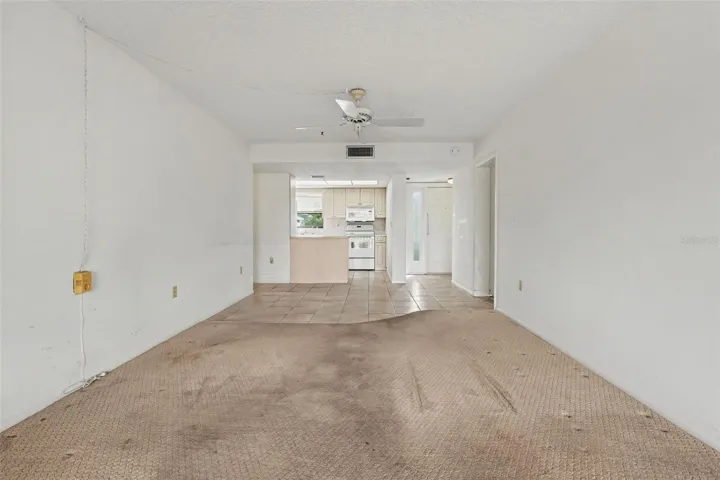 Open living and dining area looking toward the kitchen and front entry, with ceiling fan and tile flooring in the entry and kitchen.