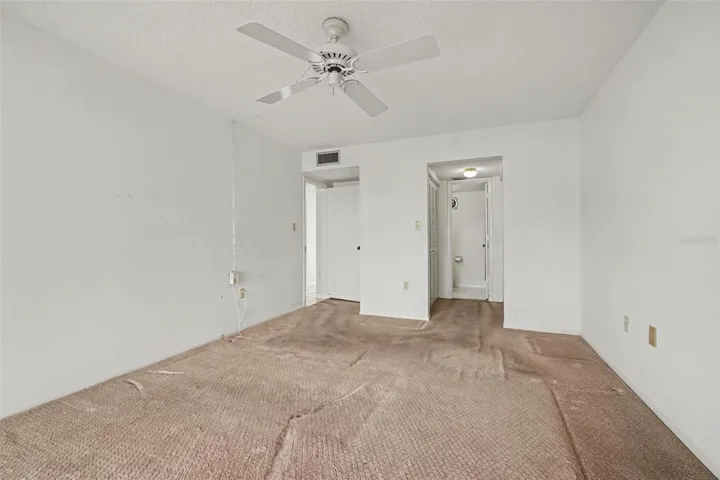Primary bedroom with ceiling fan, carpet, and direct access to the en-suite bathroom.