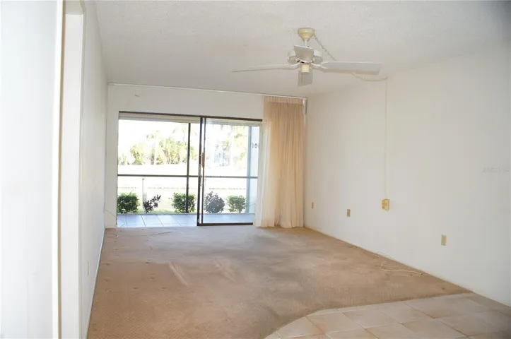 Living room with sliding glass doors opening to the screened lanai, ceiling fan, and natural light from the canal side of the condo.